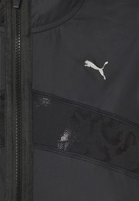 Schwarze Sportjacke mit sichtbarem Reißverschluss, strukturiertem Designstreifen und reflektierendem silbernen Logo auf der oberen linken Seite.