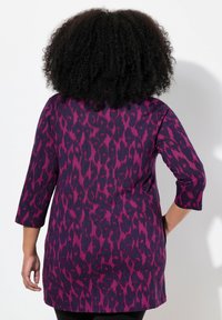 Lila tunika med ett leopardmönster i mörkare och ljusare nyanser av lila. Trekvartsärmar med rak skärning. Strukturerad tyg.