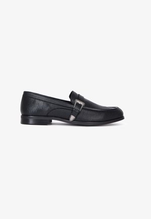 Sorte læder loafers med struktureret overflade, prydet med en sølv spænde accent og et lavt profil, designet til afslappet eller formelt brug.