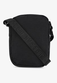 Svart axelväska tillverkad av mjukt, hållbart tyg. Rektangulär form med en justerbar rem och texturerad "OUT"-logotyp på remmen.