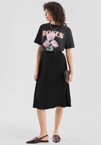 Czarna spódnica do kolan zestawiona z ciemnym t-shirtem z różowymi różami. Do tego kopertówka z ćwiekami i brązowe sandały na rzemykach.