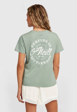 Žalios mėtos spalvos medvilninė trumpomis rankovėmis marškinėliai, nugarinėje pusėje baltas apskritas grafikas su užrašu „Banglenčių sportas yra mano terapija.“