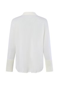 Maglione bianco a maniche lunghe con polsini a coste e colletto piccolo, mostrato da dietro su uno sfondo bianco semplice.