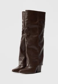 Brune læder knæhøje støvler med et slouchy design, spidse tæer og en beskeden blokhæl, der har en glat, blank finish.