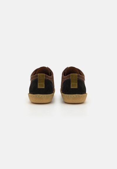 Suede shoes in black and brown, with a green accent tag at the back. Rounded sole, stitched detailing, and low-profile design.