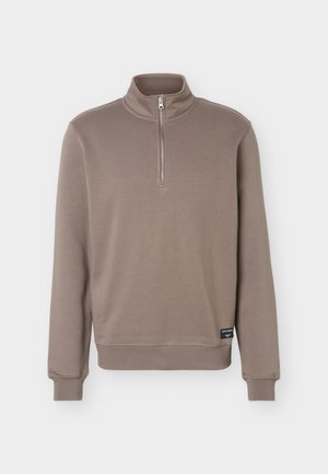 Pulover s dolgimi rokavi v barvi taupe z ovratnikom na pol-zadrgo in robovi z rebrasto pletenino, z majhno črno znamko ob robu.