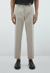 Beige skräddarsydda byxor med rak passform, som har framfickor och ett kontrasterande mörkt bälte. Bärs med svarta läderskor.