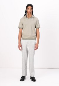 Polo de malha de manga curta verde-claro com decote em V, emparelhado com calças cinzas claras ajustadas e sapatos pretos, num modelo contra um fundo branco.