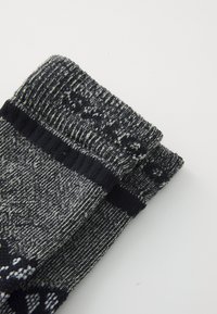 Sivé pletené ponožky s textúrovaným vzorom, s tmavým pásikom na vrchu a svetlými škvrnitými detailami po celom materiáli.