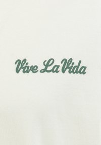 T-shirt en coton crème avec un texte cursif texturé vert foncé « Vive La Vida » centré à l'avant.