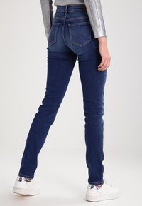 Tmavě modré skinny džíny vyrobené z denimu, s zadními kapsami a švy na detailech, spárované s bílými teniskami.