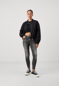 Sort bomberjakke med elastiske manchetter, cropped sort top, falmede grå skinny jeans og sorte sneakers med hvide såler og mønstrede snørebånd.
