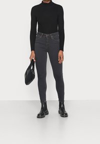Suéter negro de cuello alto acanalado, jeans skinny de cintura alta gris oscuro, botines Chelsea negros y un bolso acolchado negro.
