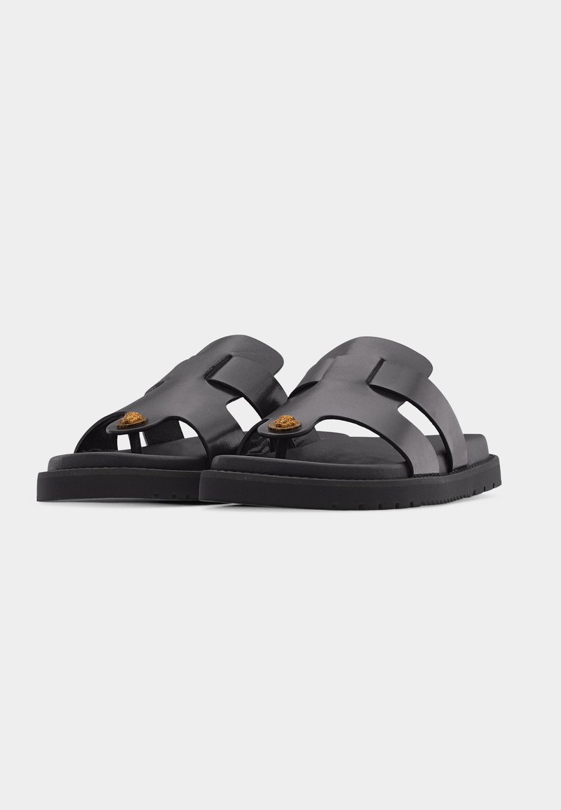 Black leather slip-on sandals with a single toe loop featuring a small brown embellishment on thick rubber soles.