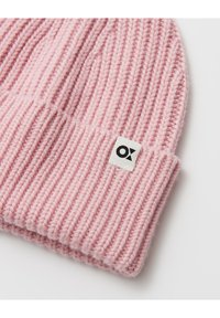 Bonnet tricoté rose avec une texture côtelée et un revers plié ; comporte une étiquette blanche avec un logo noir sur le côté.