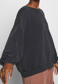 Ylimitoitettu musta collegepaita pehmeästä kankaasta, jossa on pyöreä kaula-aukko, resorit hihansuissa ja teksturoitu viimeistely.