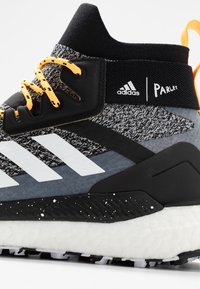 Chaussure de sport noire et grise avec des rayures blanches, des lacets orange et une tige texturée. Comprend une semelle Boost et le logo Parley.