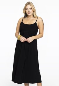 Schwarzes ärmelloses Kleid mit figurbetontem Oberteil, gerafftem Taillenbereich und fließender Midi-Länge. Glatter Stoff und minimalistisches Design.