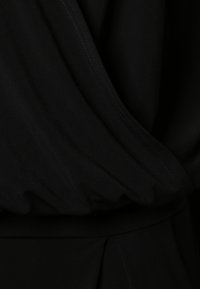 Prenda de tela negra con una textura suave, que presenta un diseño drapeado y costuras visibles que destacan su construcción en capas.