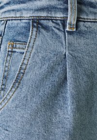 Světle modré džíny z denimu se klasickým střihem, viditelným šitím v kontrastní žluté barvě a jemnou, vybledlou texturou.