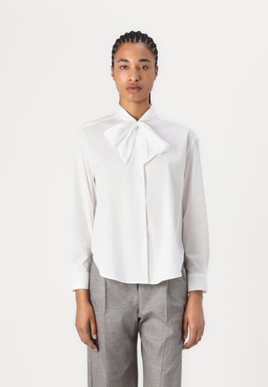 Witte blouse met lange mouwen, een strik-kraag, knopen aan de voorkant en een licht gebogen zoom, gecombineerd met grijze geruite broeken.