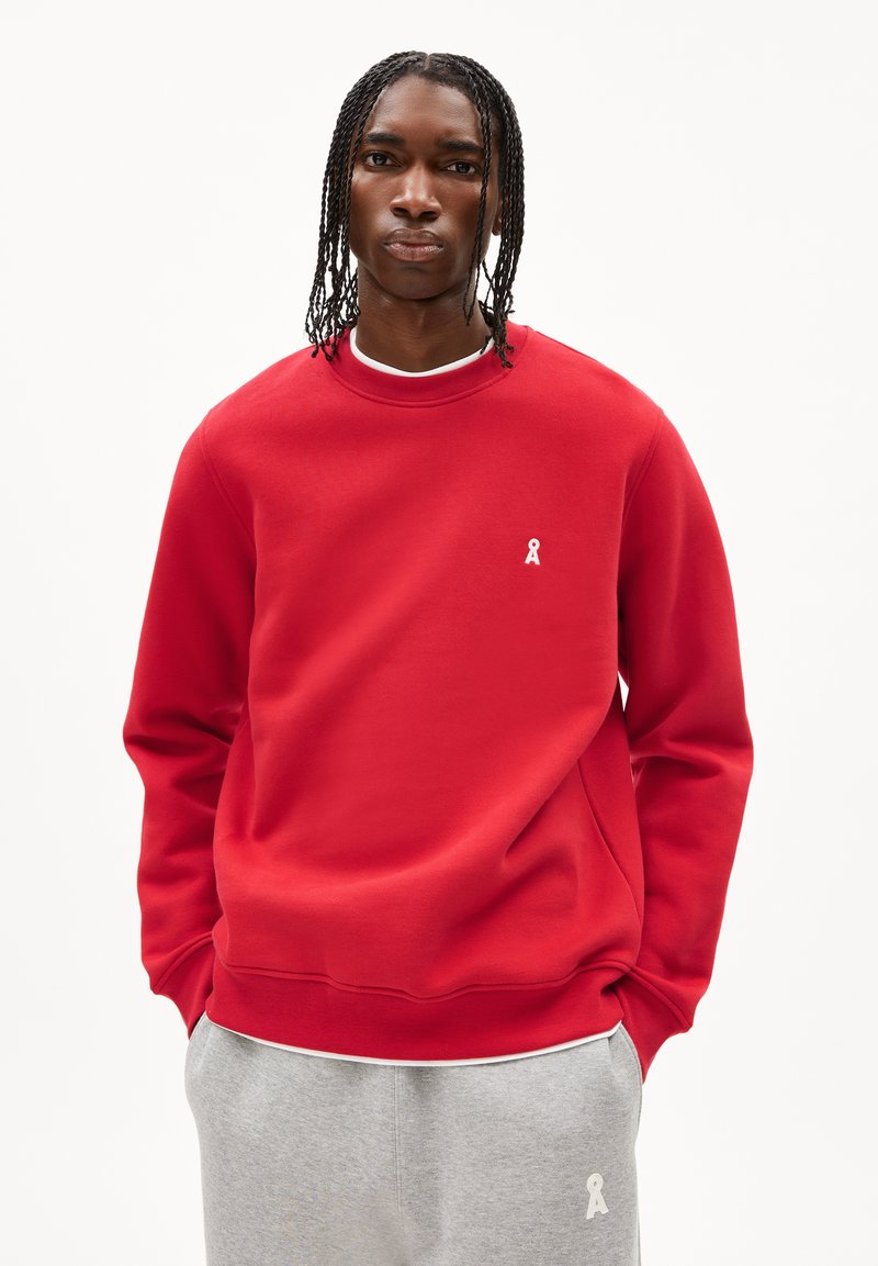 Felpa rossa in tessuto misto cotone, con scollatura a girocollo e un piccolo logo in nastro bianco sul lato sinistro del petto. La texture appare liscia.