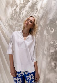 Haut blanc à col avec un décolleté en V et des manches courtes, associé à un pantalon bleu orné d'un motif blanc tourbillonnant. Tissu lisse, coupe décontractée.