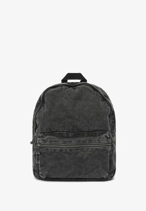 Zaino in denim nero con forma arrotondata, dotato di una tasca frontale con zip, una maniglia superiore e un tessuto texturizzato. Accenti con zip lungo le cuciture.