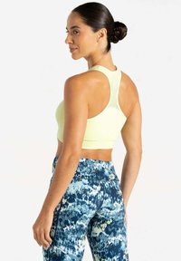 Sujetador deportivo de color amarillo claro con diseño de espalda nadadora y detalles de malla, combinado con leggings azul y blanco con patrón. Textura de tela suave.