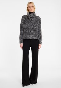 Grauer und schwarzer strukturiertes Strickpullover mit einem Schalkragen, getragen über schwarzen weit geschnittenen Hosen. Das Design zeigt eine kastige Silhouette.
