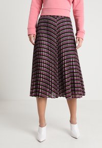 Falda negra plisada con patrones de rayas moradas y verdes, con un acabado texturizado. Combinada con un sudadera rosa y tacones blancos.
