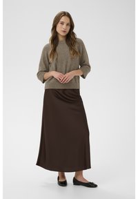 Világosbarna, rövid ujjú pulóver bordázott szegéllyel, hosszú, sötétbarna szatén szoknyával párosítva. A szettet fekete lapos cipő egészíti ki.