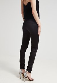 Černé skinny džíny s hladkou texturou a přiléhavým střihem, doplněné o sandály na vysokém podpatku s řemínky a hadím vzorem.