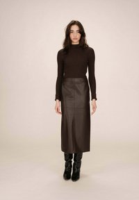 Maglione marrone a coste abbinato a una gonna midi in pelle marrone scuro. Il modello indossa stivali neri al ginocchio con tacco. Texture liscia in tutto.