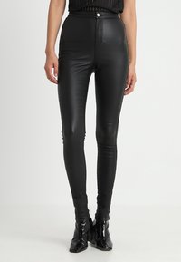 Leggings de imitación piel negra de cintura alta con una textura suave, con cierre de cremallera y botón, silueta ajustada y diseño elegante.