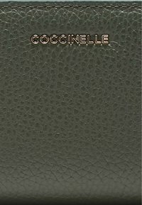 Portafoglio in pelle verde con finitura testurizzata, logo dorato "Coccinelle" e linee pulite. Design compatto adatto a vari usi.