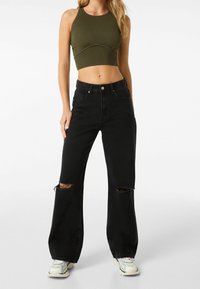 Mustat revityt farkut korkeavyötäröisinä, yhdistettynä tummanvihreään ribbikuvioiseen crop-toppiin. Denimissä on rosoiset reunat ja näkyvä ommel.