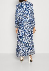 Sukienka maxi w niebiesko-białym wzorze zebra, z długimi rękawami, elastycznymi mankietami i warstwowym falbaniastym dołem. Wykonana z lekkiego materiału.
