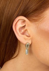 Boucles d'oreilles pendantes en ton or, composées de deux pierres rectangulaires, dont l'une avec un bord clair, présentant un design épuré et une finition polie.