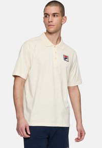 Polo de manga corta en beige de algodón con tapeta de botones y logo bordado en el lado izquierdo del pecho. Textura suave, ajuste clásico.