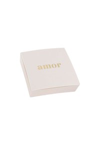 Scatola quadrata, di un morbido colore rosa, con una finitura liscia, su cui è impresso la parola "amor" in lettere dorate sulla superficie superiore. Design pulito e minimal.