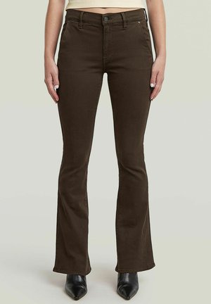 Bruine hoge taille wijde broek gedragen met zwarte puntige laarzen, getoond van taille tot voeten tegen een effen lichte achtergrond.