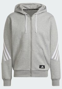 Felpa con cappuccio grigia con cerniera, cappuccio con coulisse, dettagli con tre strisce bianche sulle maniche, tasche frontali e piccolo logo Adidas nero sull'orlo.