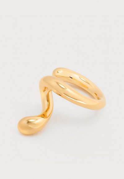 Δαχτυλίδι από ματ μέταλλο σε χρυσή απόχρωση, με αφηρημένο, κυματιστό σχέδιο που καταλήγει σε σχήμα σταγόνας, σε λευκό απλό φόντο.