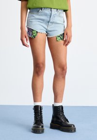 Denim šorti ar saplēstiem maliem, gaiši zila krāsa, ar kr�āsainu rakstainu audumu, kas iznāk no sāniem. Valkāti ar melniem šņorējamiem zābakiem.