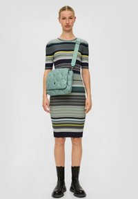 Gestreiftes Strickkleid in Grün, Marineblau und Gelb. Teal-farbenes, gesteppte Schultertasche mit runder Form. Schwarze Knöchelstiefel mit einer klobigen Sohle.