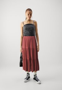 Débardeur en denim noir avec des clous, jupe maxi rouge à volants, baskets montantes noires, portant un petit sac à main noir.