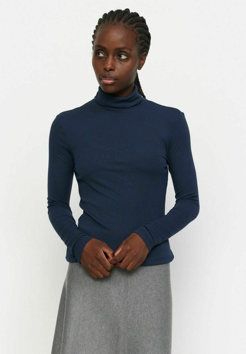 Navy turtleneck long-sleeve top in ribbed fabric, fitted design with smooth texture, paired with a gray skirt.