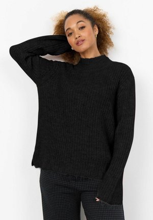 Svart stickad pullover med hög krage, lång ärm och lös passform. Har ribbad textur och ofärdiga fållar.