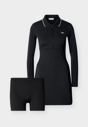 Svart langermet polokjole med glidelås foran og hvit kant på kragen, kombinert med svarte tettsittende shorts.